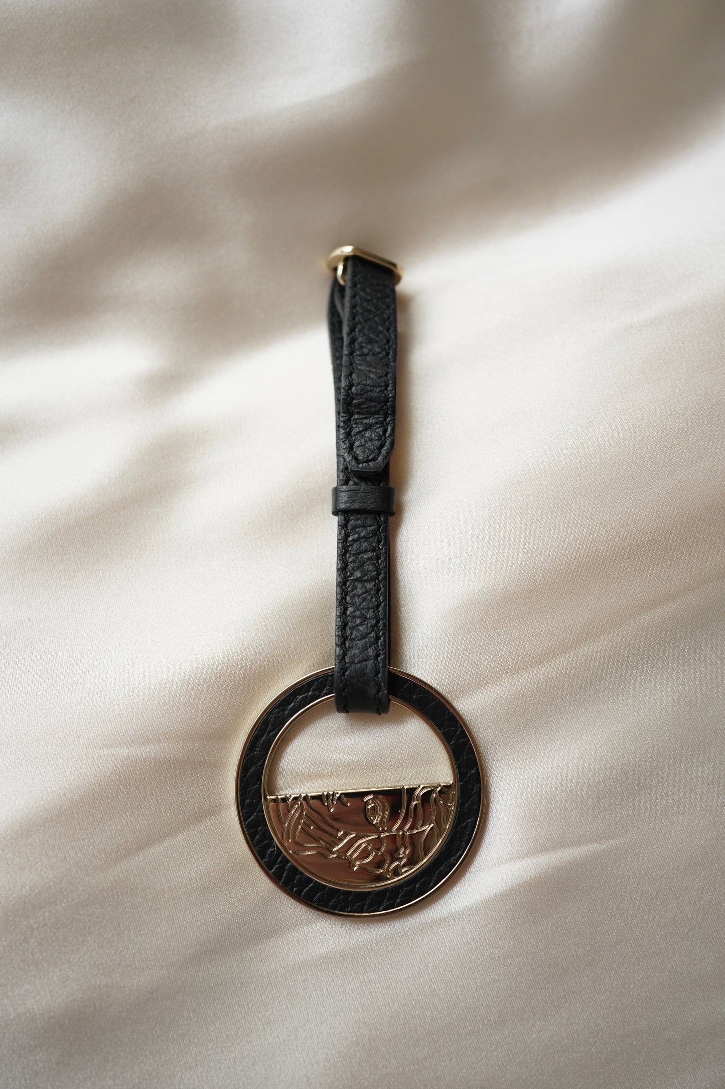 Black leather keychain with a circular metal tag on a light fabric background