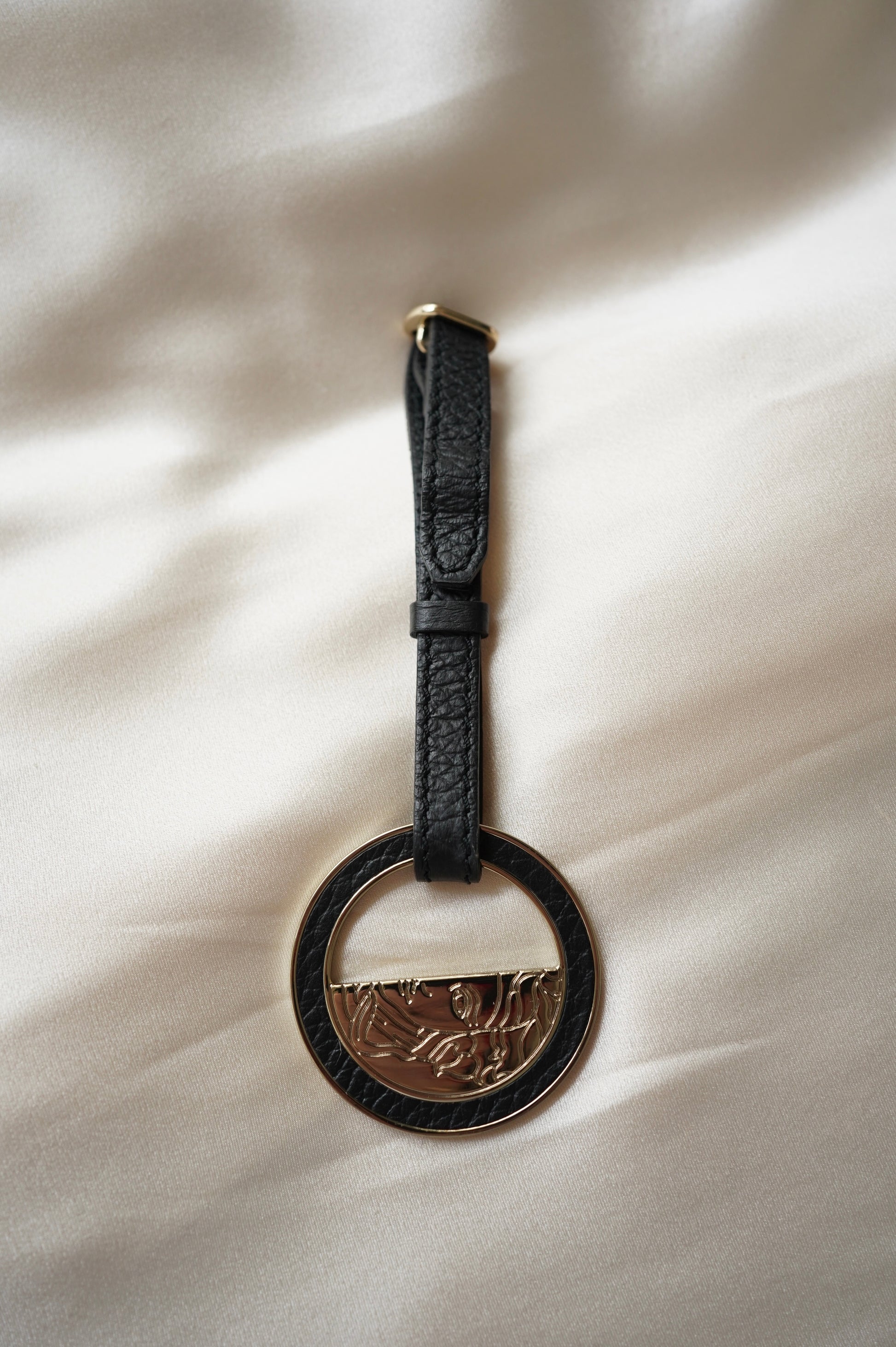 Black leather keychain with a circular metal tag on a light fabric background