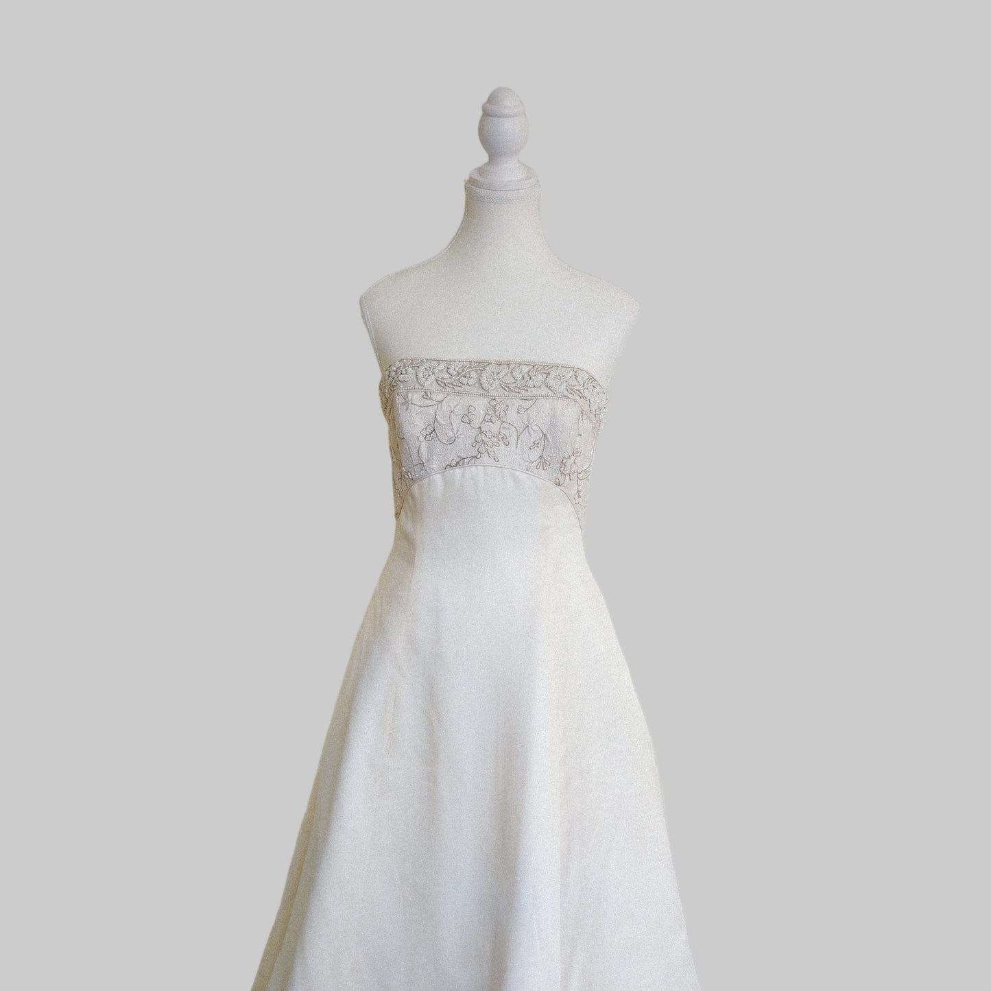 White wedding dress on a mannequin against a plain white wall.