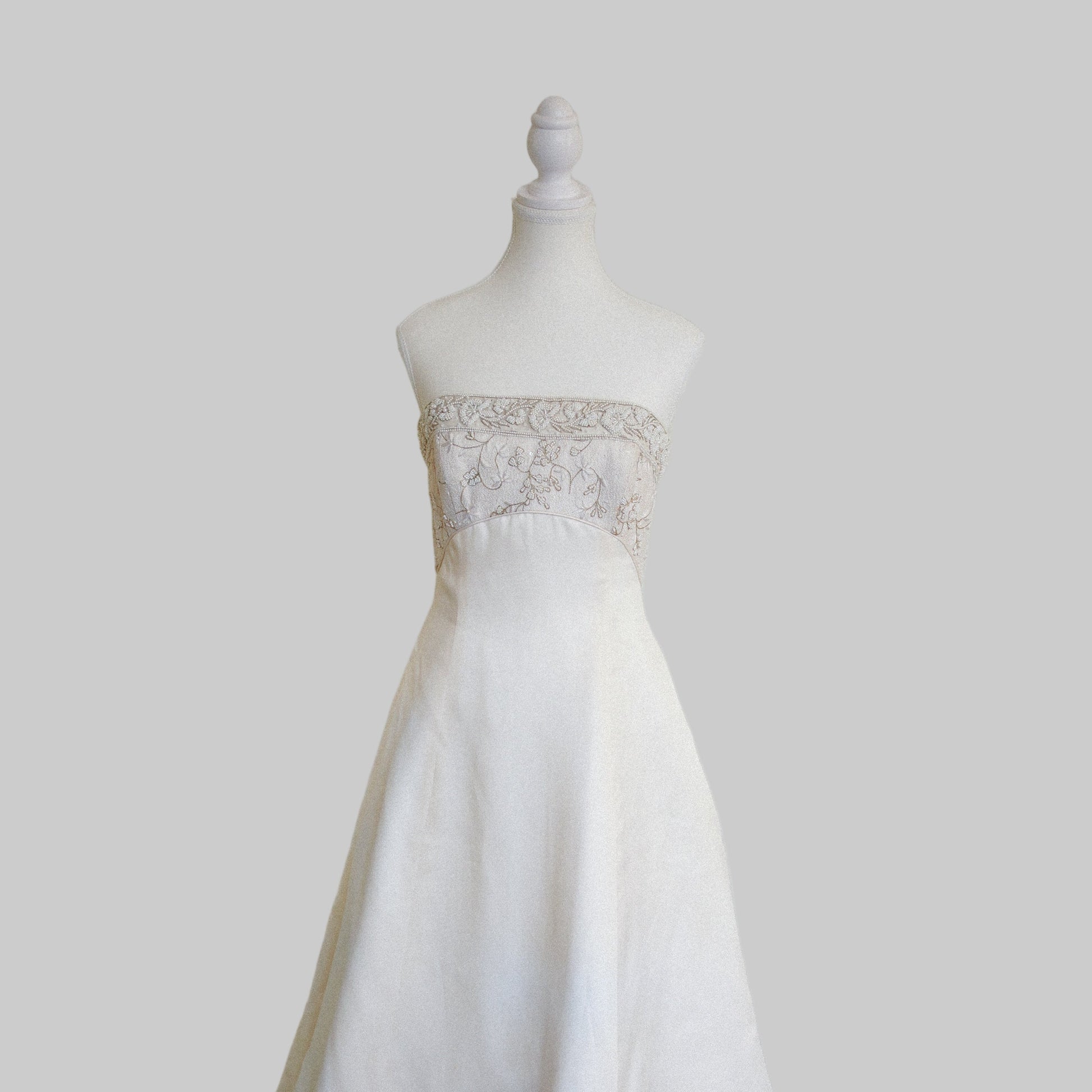 White wedding dress on a mannequin against a plain white wall.